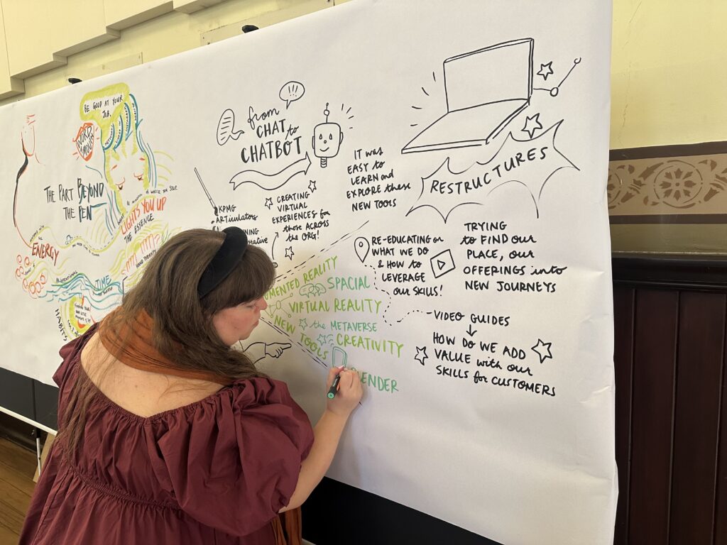 Kate Baxter in the middle of graphic recording the closing keynote presentation by Phil Marsden and Kenneth Chung from KPMG Articulators